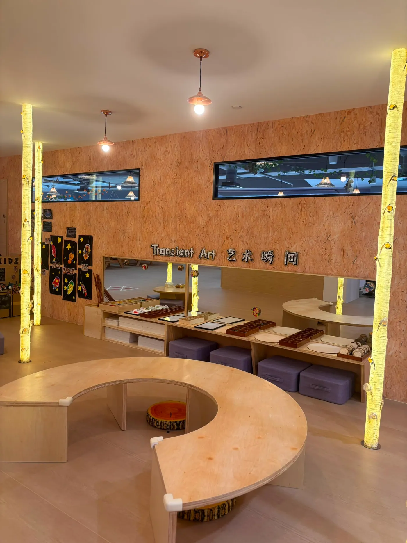 A serene loose-parts art studio with glowing birch columns and round plywood seating